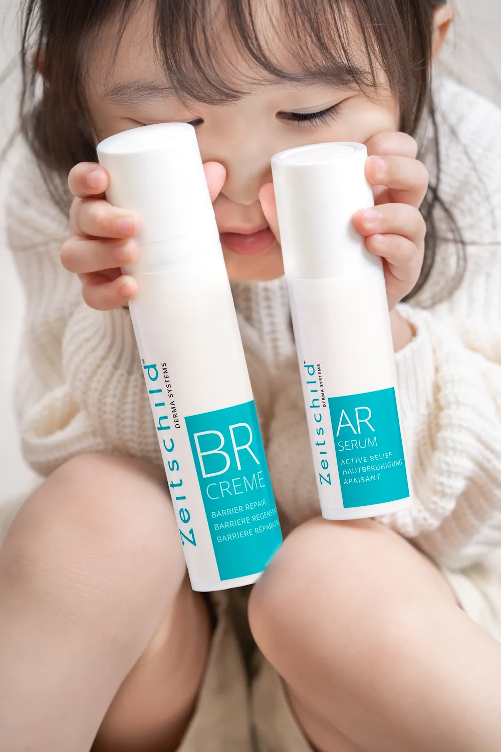 Young child holding Zeitschild BR Creme and AR Serum bottles